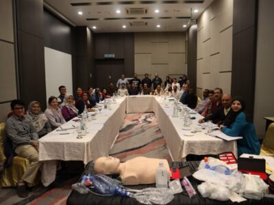 Face-to-face-Medical Training Session with Healthcare Professionals - MRCEMMASTER Group of medical professionals gathered in a conference room for a training session, with simulation equipment displayed on a table.