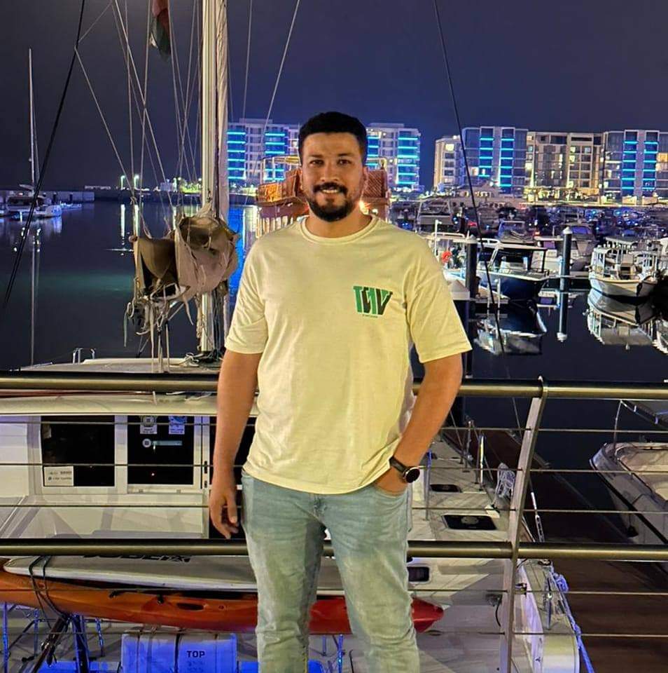 Public Relations Coordinator for MASTERFRCEM LLC standing by a marina at night, with boats and a lit-up cityscape in the background.